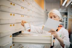 En apotekare plockar medicin ur en låda i ett apoteksförvaringssystem.