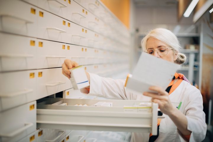 En apotekare plockar medicin ur en låda i ett apoteksförvaringssystem.