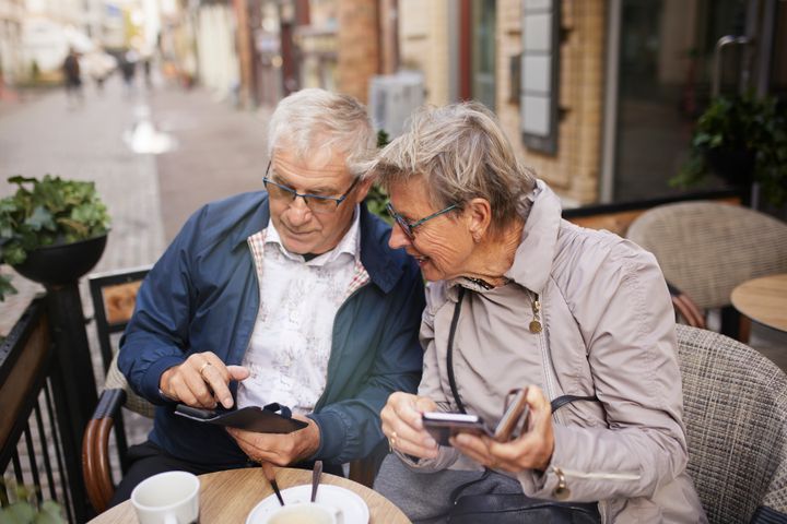 Ett äldre par tittar på varsin smartphone i offentlig miljö.
