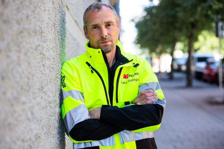Lars Hildingsson, tf förbundsordförande Byggnads, i gul reflexjacka lutar sig mot en vägg utomhus.