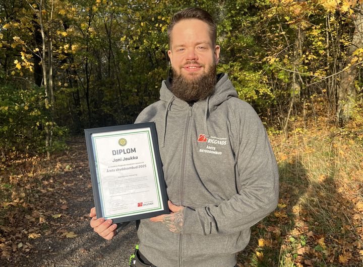 En man i grå huvtröja står utomhus och håller ett diplom för Årets skyddsombud från Byggnads Stockholm-Gotland.