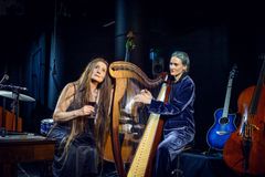 Två kvinnor sitter vid en harpa, ena spelar och ena lyssnar harmoniskt på musiken.