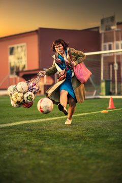 Arg kvinna som bär massor sparkar argt en fotboll på en fotbollsplan.