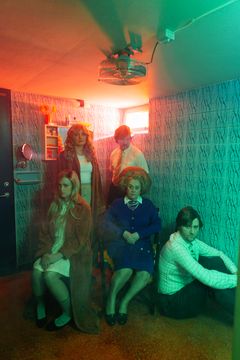 Fem personer sitter i ett badrum med röd och grön belysning. Suggestiv stämning.