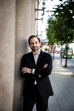 En man i kostym lutar sig mot en pelare på en trottoar.