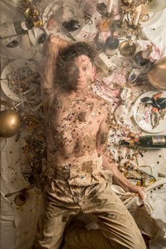 En person ligger på ett smutsigt bord fyllt med rester från en fest.