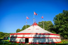 Teatertältet i Gottsunda, ett stort cirkustält med röd och vit design, omgivet av grönska och blå himmel.