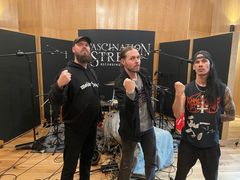 Grupp av tre personer poserar framför musikinstrument i en inspelningsstudio.