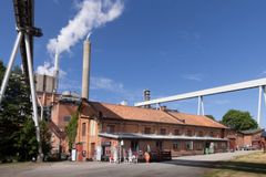 Brun tegelbyggnad med industriskorstenar och rök, del av Frövifors Pappersbruksmuseum på en solig dag.