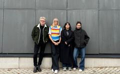 Fyra personer står uppradade mot en vägg och kollar in i kameran