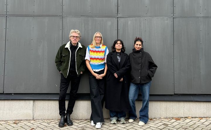 Fyra personer står uppradade mot en vägg och kollar in i kameran