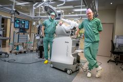 Två läkare står intill en operationsrobot.