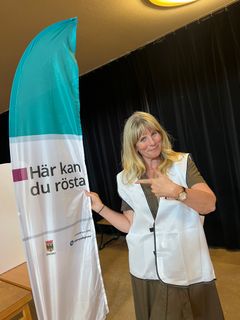 Blond leende kvinna bredvid beachflagga med texten Här kan du rösta.