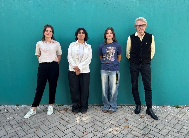 Gruppfoto av fyra personer som står framför en turkos vägg.