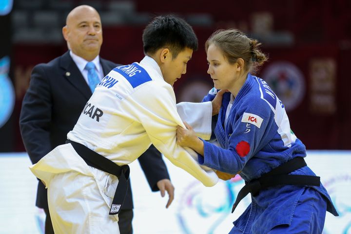 Nicolina och hennes motståndare håller i varandra i dräkterna. En domare står bakom dem och bedömmer matchen.