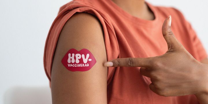 En person pekar på ett plåster på sin arm som säger "HPV-vaccinerad".