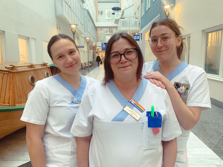 Tre personer i sjukhuskläder står tillsammans i en ljus korridor på Sunderby sjukhus.