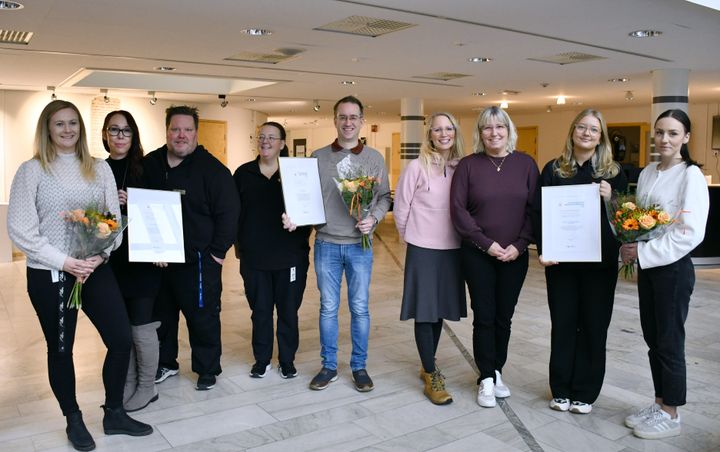 En grupp människor poserar inomhus med blommor och diplom.