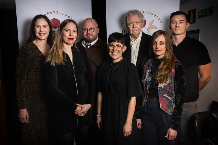 En grupp sju personer står tillsammans framför en skylt med texten "Kulturtipendium".