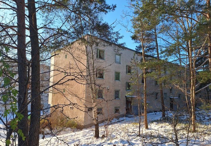Flerbostadshus i Stockholmsförort, fotograferat från en snöig skogsglänta.