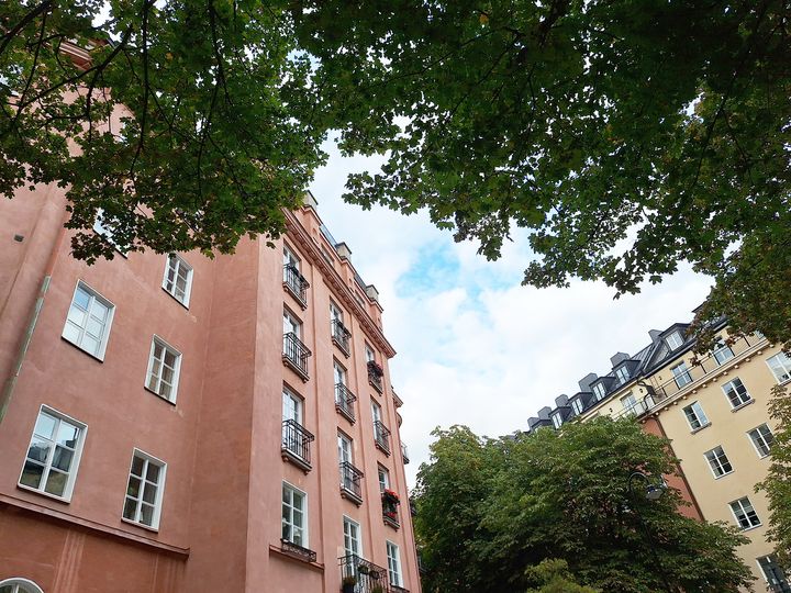 Flerbostadshus i stadsmiljö, inramade av träd och himmel.