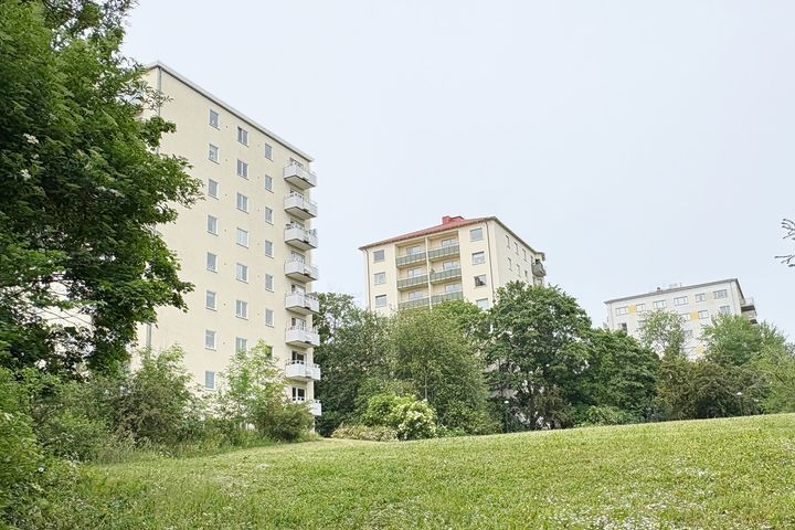 Tre flerbostadshus med blekblå himmel i bakgrunden och blekt gräsmatta i förgrunden