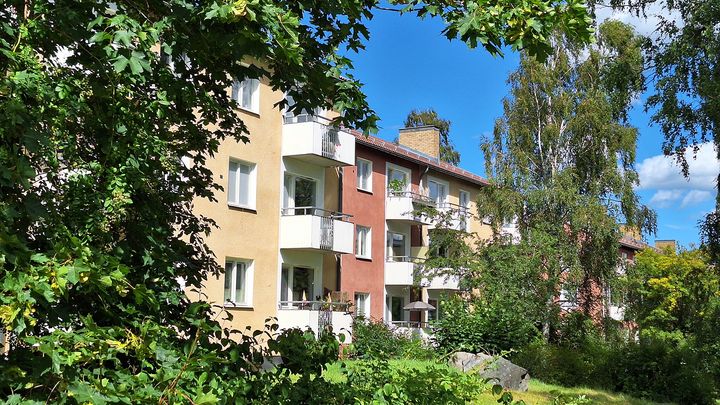 Flerbostadshus i sommargrönska mot blå himmel