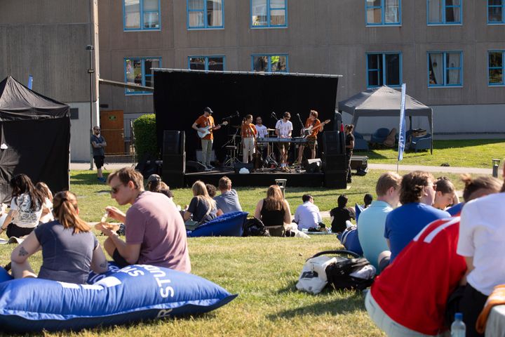 En grupp studenter uppträder på en utomhusscen medan folk sitter på gräset och tittar på.