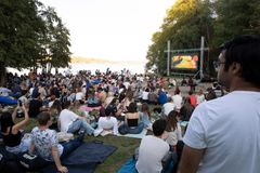 En stor grupp människor sitter utomhus på filtar vid Lappis Beach och tittar på en biofilm på en stor skärm.