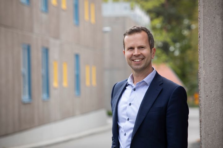 Stockholms studentbostäders Vd Mattias Carrass står utomhus framför en byggnad med grå fasad och gula fönster.