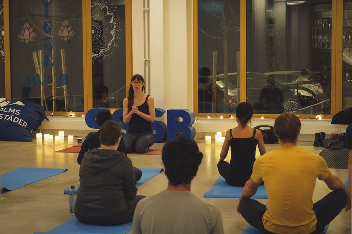 En instruktör undervisar en yogaklass i en väl upplyst studio med yogamattor och tända ljus.