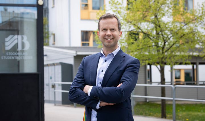 Mattias Carras, vd stockholms studentbostäder i kostym står utomhus framför en byggnad och ler.