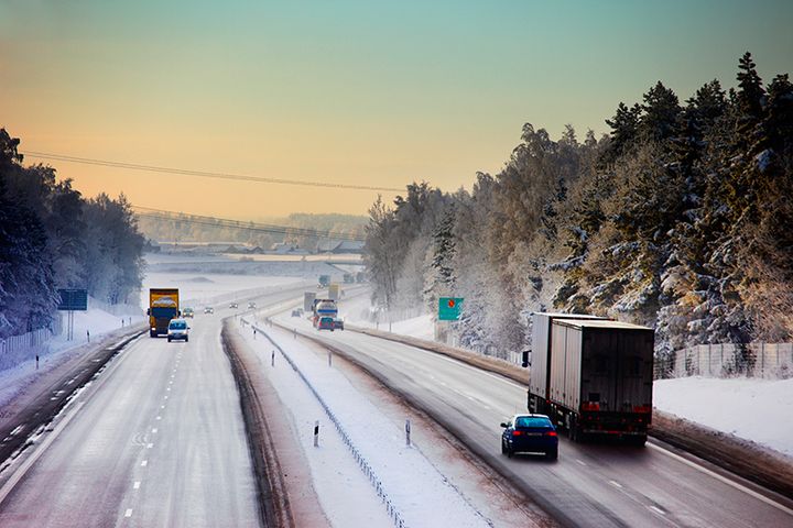En motorväg i ett vintrigt skogslandskap där bilar och lastbilar kör.