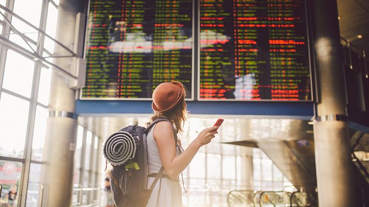 Resenär framför en avgångstavla på flygplats.