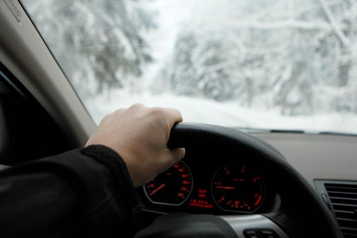 Närbild på hand och ratt, i bakgrunden ett vintrigt landskap som syns genom vindrutan.