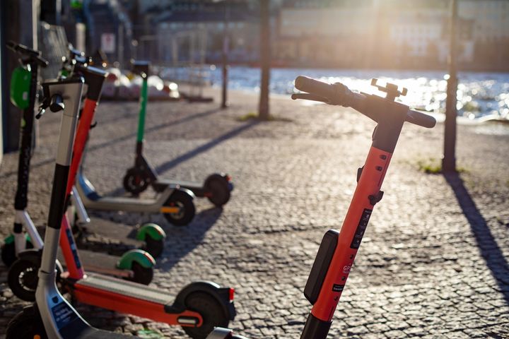 Alt text: Flera elsparkcyklar står parkerade på en stenbelagd trottoar vid vattnet.