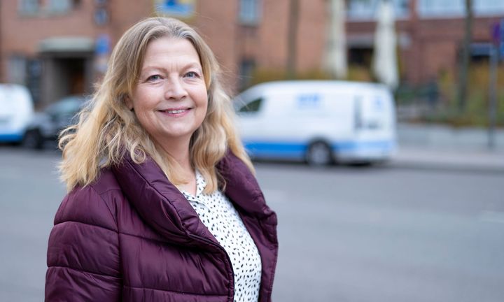 Foto på Charlotte i blus och lila täckjacka utanför kontoret med Einar Mattsson-bilar i bakgrunden