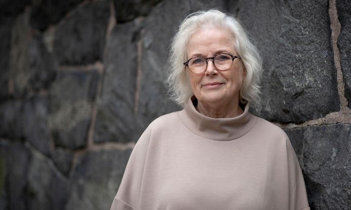 Bild på Gunilla i beige tröja framför en grå mur utomhus