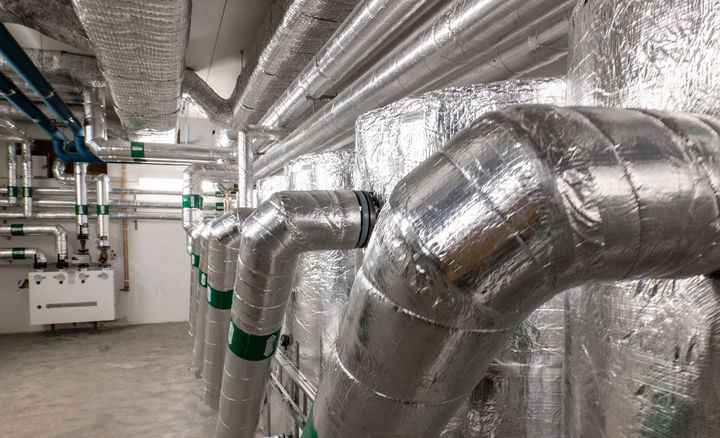 Bild på folieinpackade rör och elkopplingar i ett teknikrum under en fastighet