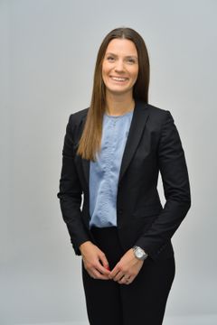 Emma i svart kostym med ljusblå blus under mot grå bakgrund