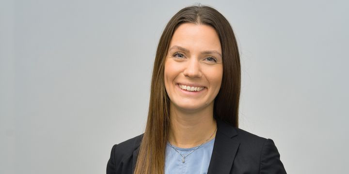 Emma i svart kavaj med ljusblå blus under mot grå bakgrund