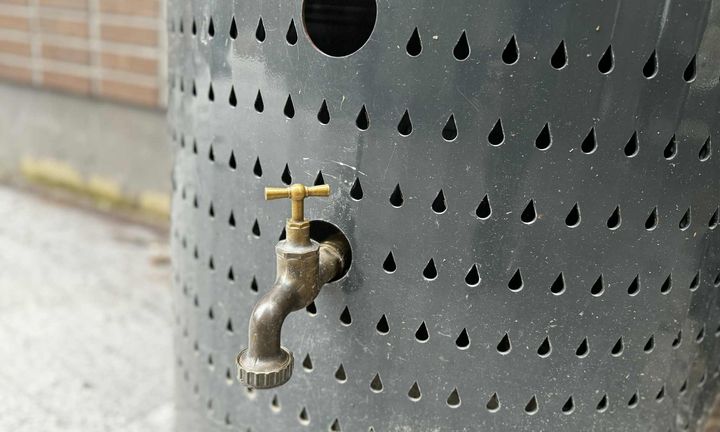 Bild på en grå uppsamlare för dagvatten med en kopparfärgad ventil framtill.