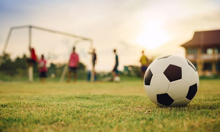 Fotboll i förgrunden och spelare kring ett mål i bakgrunden