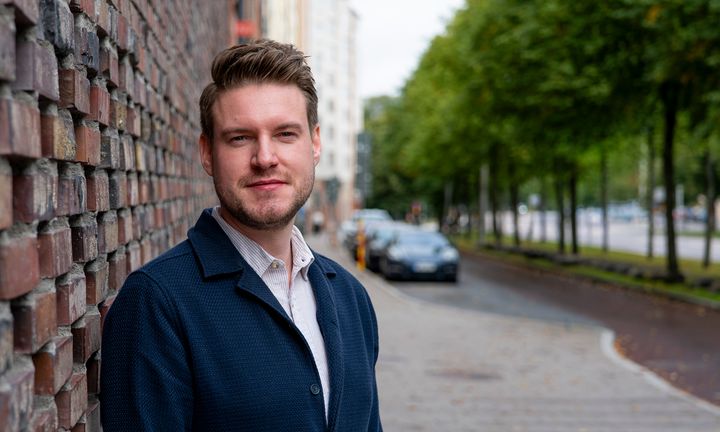 Foto på Lucas i svart jacka framför rödfärgad tegelmur utomhus