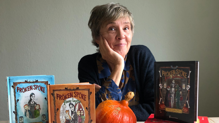 Författaren sitter vid ett bord med böcker och en pumpa.