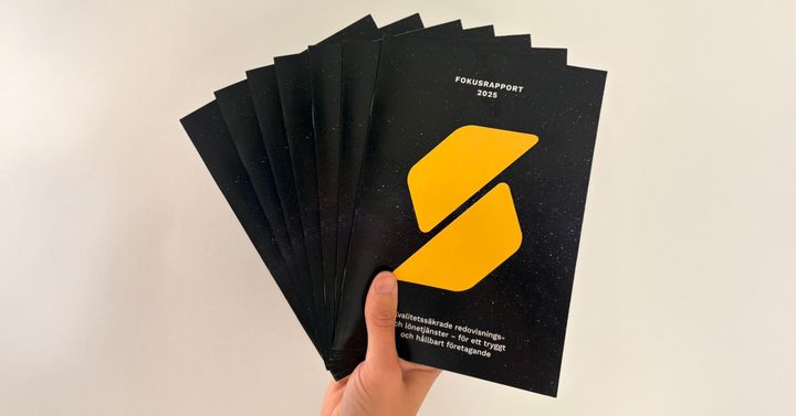 En hand håller upp en bunt av årets fokusrapport mot en neutral bakgrund.