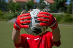 Barn med fotbollshandskar håller en fotboll framför ansiktet