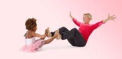 En kvinna och ett barn sitter mittemot varandra och balanserar med händerna i luften och benen sträckta framför sig.