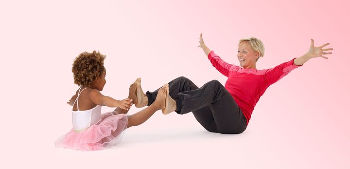 En kvinna och ett barn sitter mittemot varandra och balanserar med händerna i luften och benen sträckta framför sig.