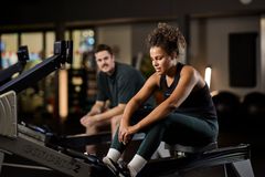Två personer pausar i träningen på varsin roddmaskin i gymmet.